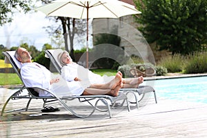 Man and woman relaxing in long chairs near pool