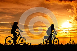 A man and a woman ride bicycles on the road with beautiful colorful sunset sky