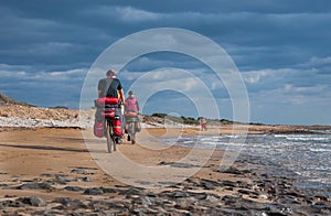 Man and woman riding sandy beach mountain bike with backpack.
