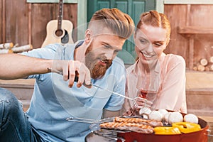 Man and woman roasting meat and vegetables on barbecue grill