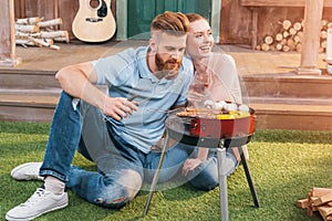 Man and woman roasting meat and vegetables on barbecue grill