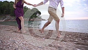 A man and a woman running along the pebble beach holding hands