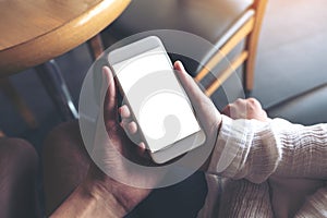 Man and woman`s hands holding and looking at white mobile phone with blank desktop screen together