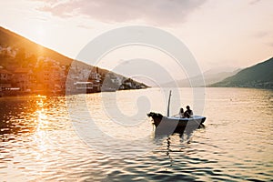 Man and woman are sailing in a boat with oars on the sea against the sunset sky