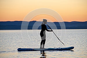 A man and a woman are sailing on a sapa along a mountain lake against the backdrop of sunset. Active family recreation for a healt