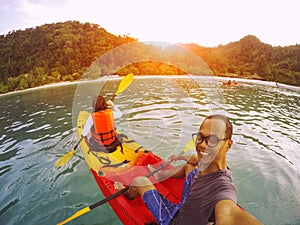 Man and woman sailing sea kayak over clear water of island