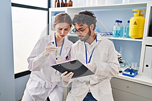 Man and woman scientist partners looking test tube holding clipboard at laboratory