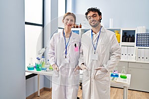 Man and woman scientist partners smiilng confident standing at laboratory