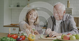 Man and woman senior couple cooking salad and checking recipe with smartphone in kitchen at home