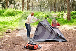 A man and a woman are setting up a tent in a forest.