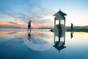 Man and woman silhouettes coming in the rays of the setting sun on landscape of beautiful infinity pool and sea and oriental
