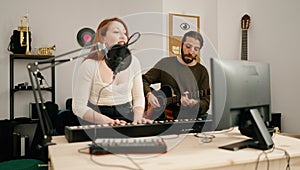 Man and woman singing son playing guitar and keyboard piano at music studio