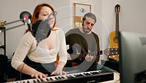 Man and woman singing son playing guitar and keyboard piano at music studio