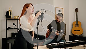 Man and woman singing son playing guitar at music studio