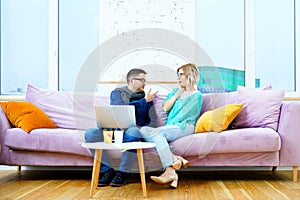 Man and woman sit on the couch, chatting and using a desktop computer.