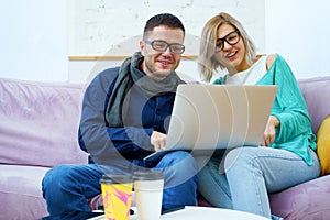 Man and woman sit on the couch, chatting and using a desktop computer.