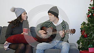 Man and woman sit sofa playing guitar singing song