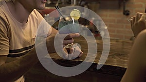 Man and woman sitting at bar counter and drinking alcoholic cocktail while evening date in cafe. Young couple drinking