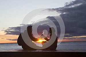 A man and a woman sitting on the beach at sunset and drinking wine