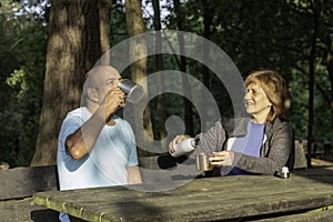 Man and woman sitting on a bench rehydrating with water in a metal cup after trekking in the mountains