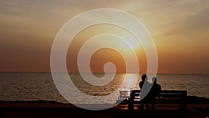 Man and woman sitting on the bench watching the sunset on the sea