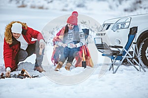 man with woman sitting on chairs near camp fire in winter time. car travel.