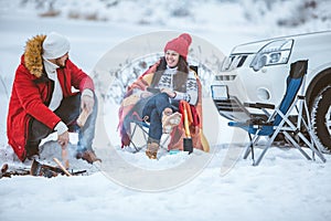 man with woman sitting on chairs near camp fire in winter time. car travel.
