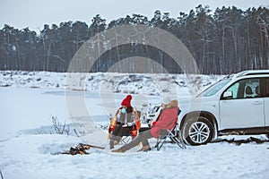 man with woman sitting on chairs near camp fire in winter time. car travel.