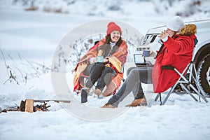 man with woman sitting on chairs near camp fire in winter time. car travel.