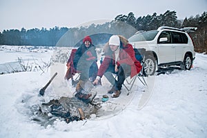 man with woman sitting on chairs near camp fire in winter time. car travel.