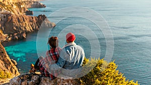 A man and a woman are sitting on the edge of a cliff by the sea. Honeymoon. Honeymoon trip. Man and woman at the sea.