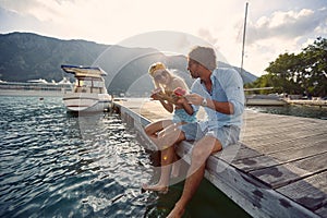 Man and woman sitting on the lake pier dangling legs and eat watermelon