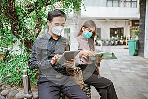 man and woman sitting on the park bench with tablet