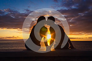 Man and woman sitting by the sea kiss at sunset