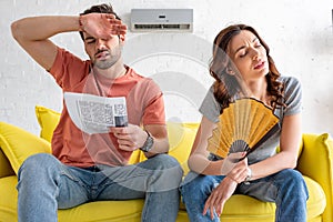 Man and woman sitting on sofa and suffering from heat at home