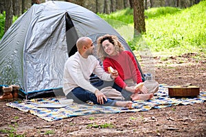 A man and woman are sitting in a tent, eating sandwiches.