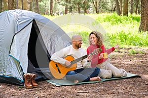 A man and woman are sitting in a tent, playing a guitar.