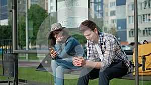 Man and woman are sitting together at transport station. They are holding modern gadgets and entertaining with internet