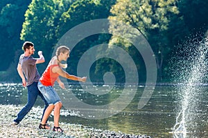 Man and woman skimming stones on river