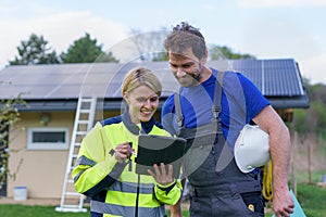 Man and woman solar installers engineers with tablet while installing solar panel system on house.