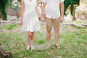 Man and woman stand side by side in the park on the grass and hold hands