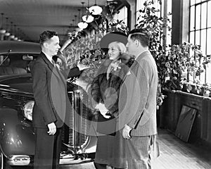 Man and woman standing in a car showroom talking to a salesman