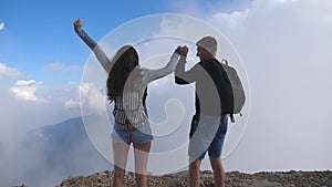 Man and woman standing on the edge of beautiful canyon, victoriously outstretching arms up. Young couple of tourists