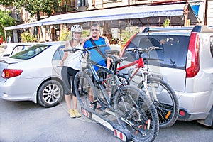 Man and woman are standing near two bicycles mounted on trunk of