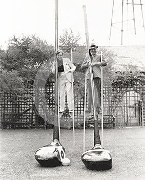 Man and woman on stilts holding giant golf clubs