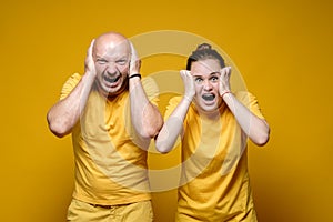 Man and woman are in stress, they cover their ears with their hands and scream hysterically. Yellow background.