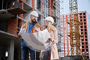 Man and woman studying building plan at construction site.