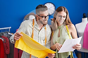 Man and woman tailors holding cloth looking clothing design at clothing factory