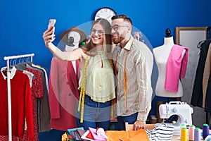 Man and woman tailors smiling confident make selfie by smartphone at clothing factory