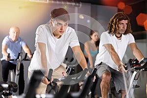 Man and woman taking indoor cycling class at fitness center, doing cardio riding bike